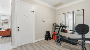 Une salle de sport à domicile équipée d’un tapis de course, d’un banc de musculation et d’haltères.