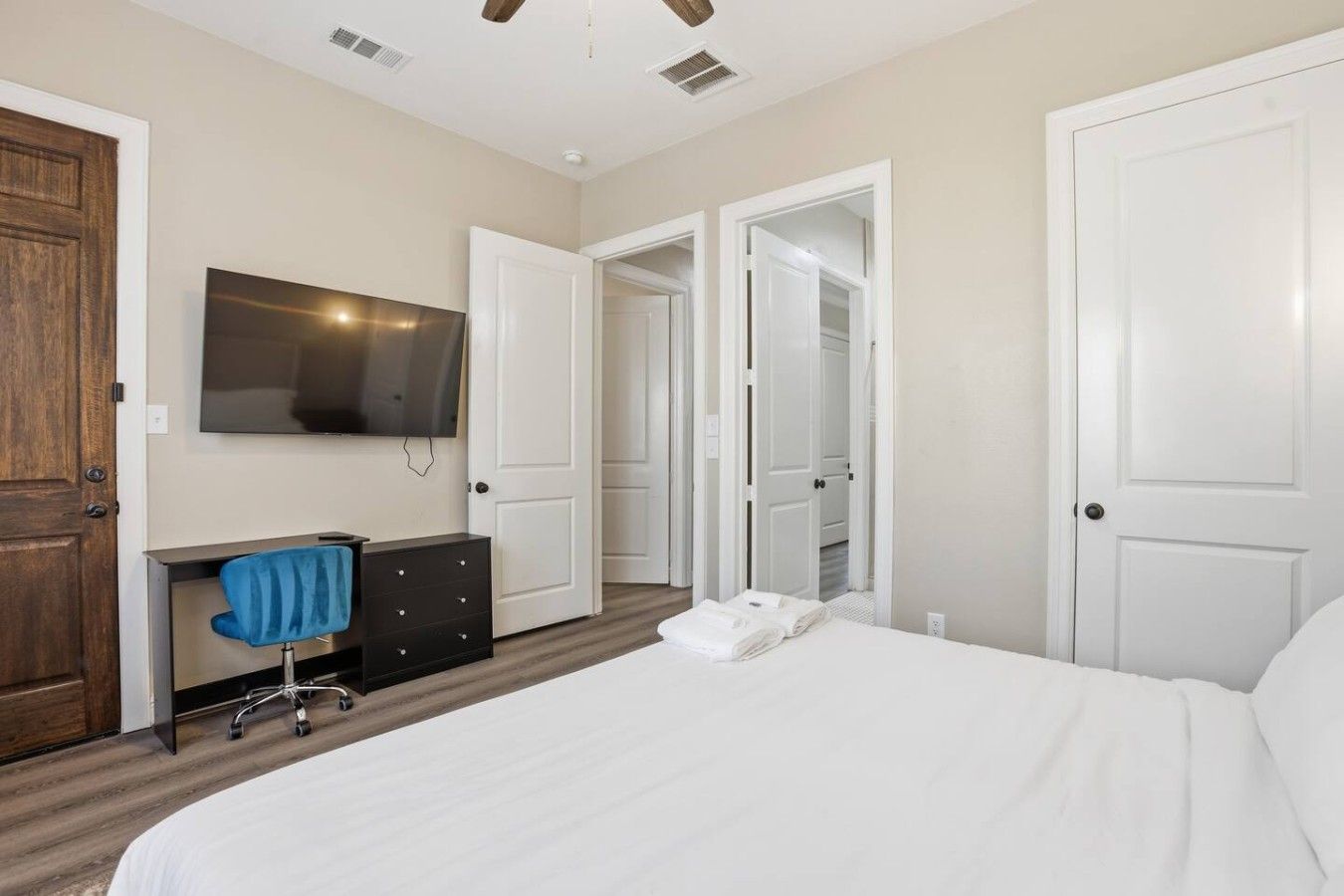 A bedroom with a bed, a desk with a chair, a television, and two doors.
