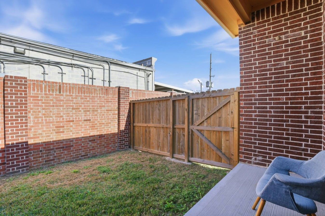 A backyard with a brick wall, a wooden fence, and a patio area with a chair.