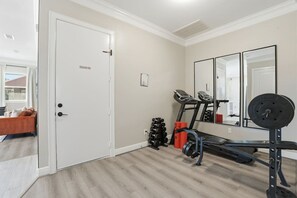 Une salle de sport à domicile équipée d’un tapis de course, d’un banc de musculation et d’haltères.