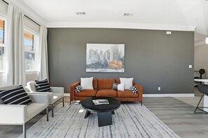 Un salon moderne avec un canapé, des fauteuils, une table basse et un tableau représentant un paysage urbain accroché au mur.