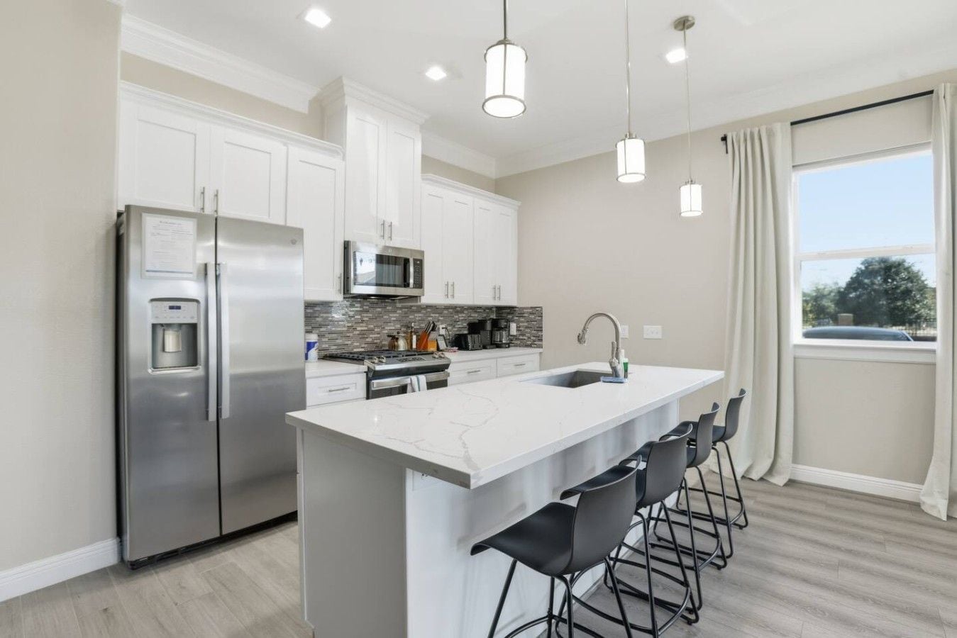 A modern kitchen with a stainless steel refrigerator, a microwave, and a large island with bar stools.