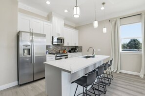Una cocina moderna con un refrigerador de acero inoxidable, un microondas y una isla grande con taburetes de bar.