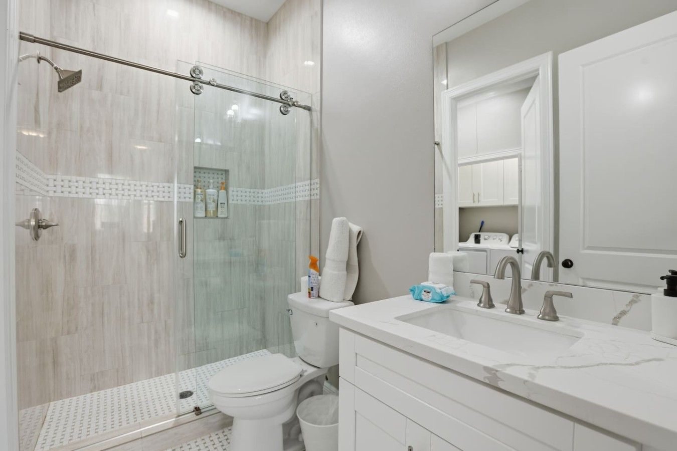 A modern bathroom with a glass-enclosed shower, a white toilet, and a sink with a mirror above.