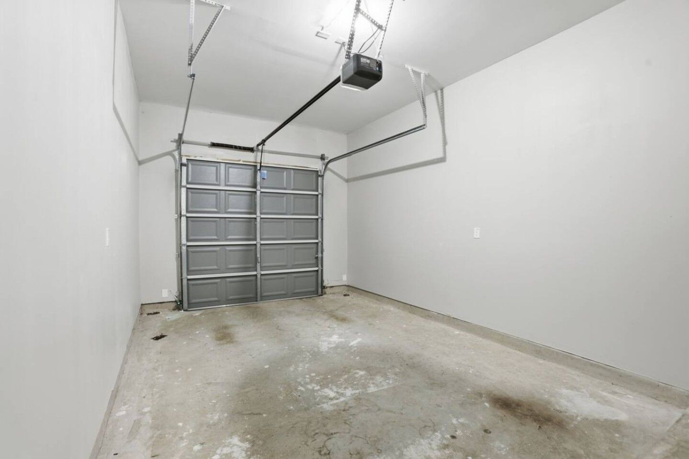 Ett garage med en stängd metalldörr, betonggolv och takbelysning.