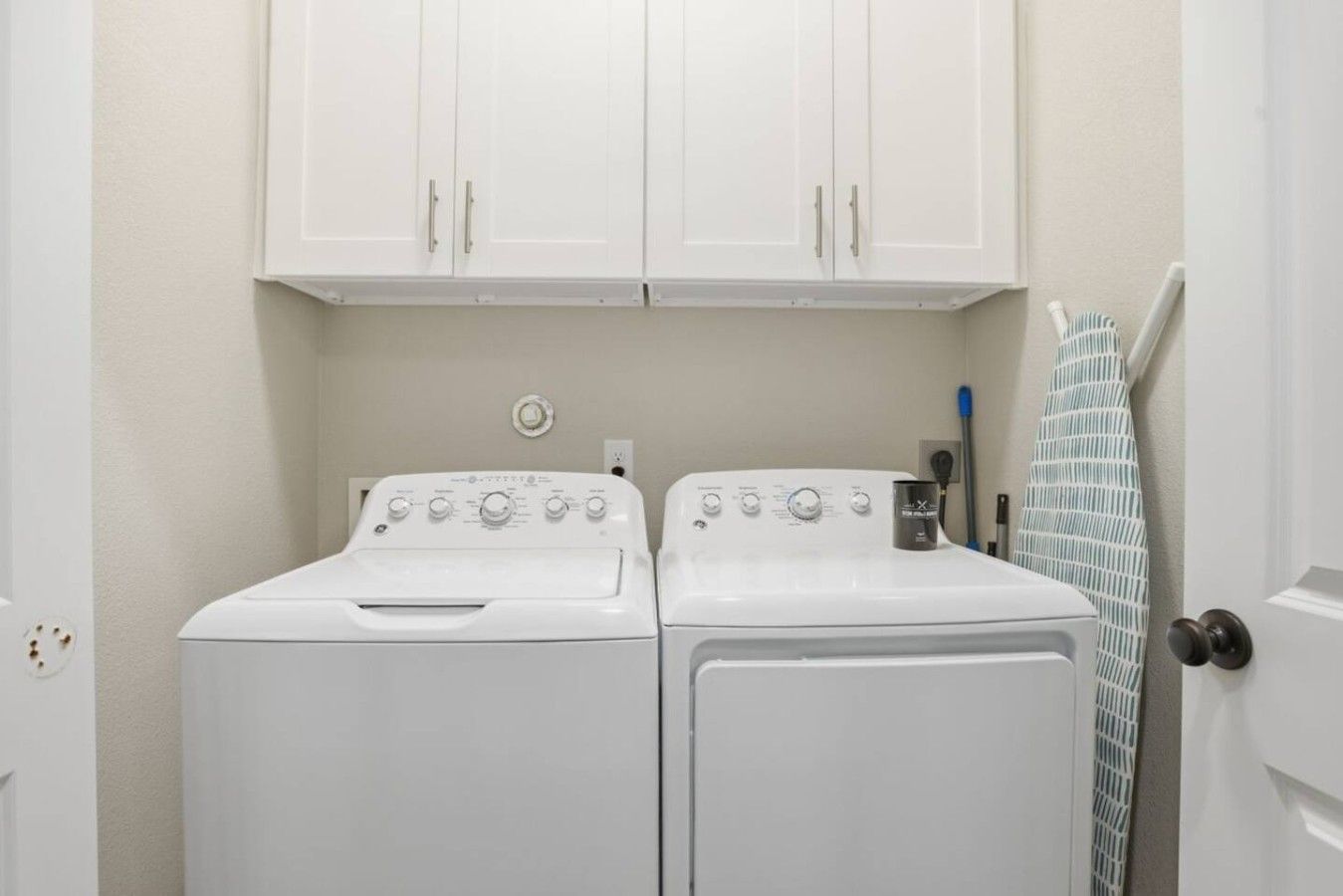 A laundry room with two white front-loading washers and dryers, a towel rack, and a door with a towel hanging on it.