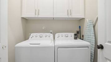 A laundry room with two white front-loading washers and dryers, a towel rack, and a door with a towel hanging on it.