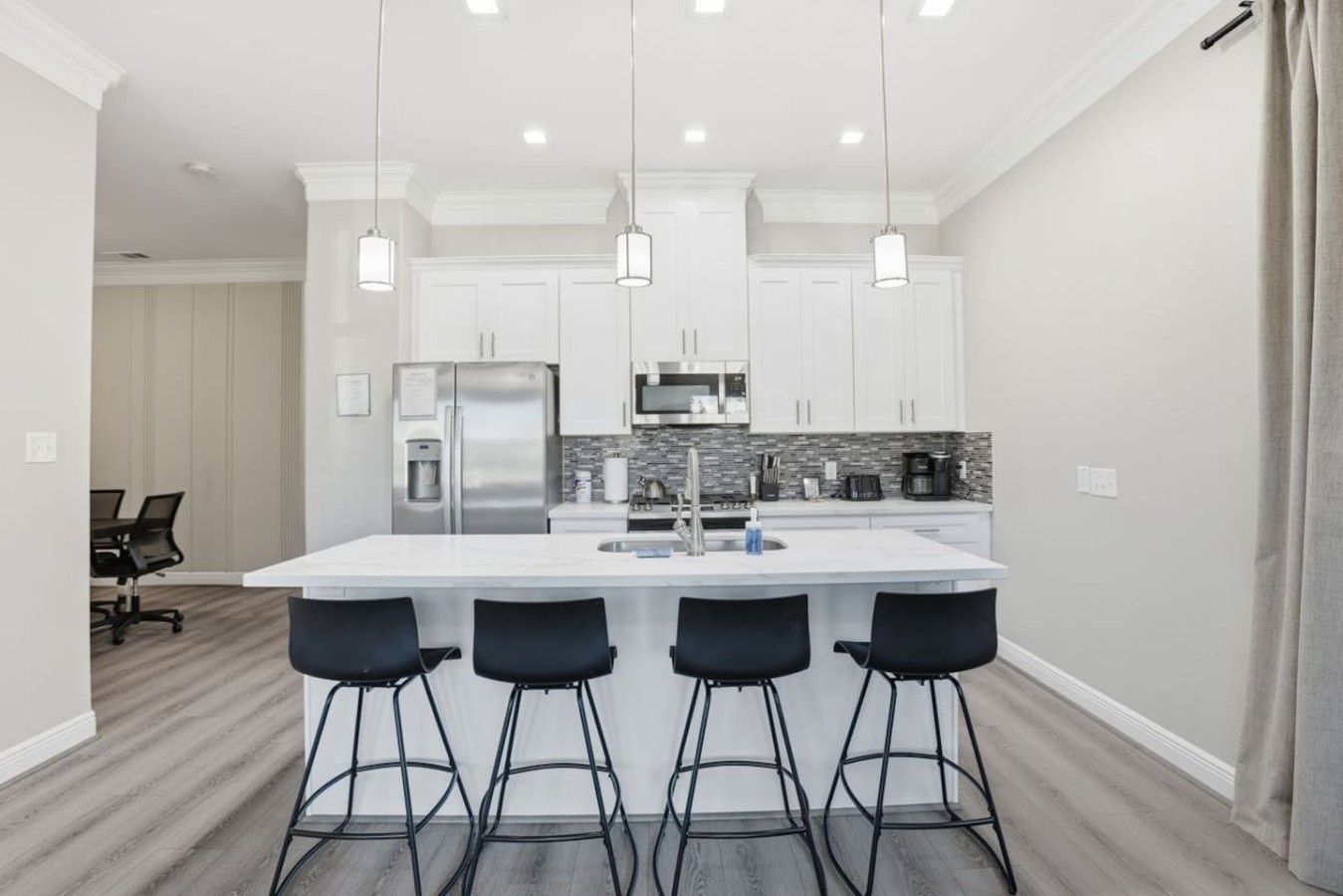 A modern kitchen with a central island, bar stools, stainless steel appliances, and pendant lighting.