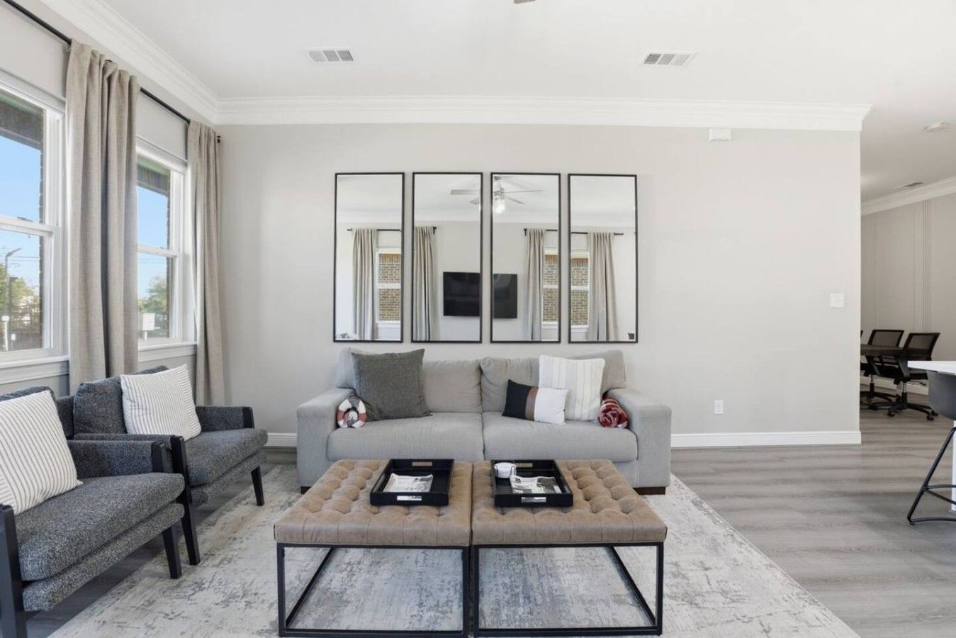 A modern living room with a grey sofa, two armchairs, a coffee table, and a large mirror on the wall.