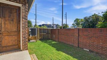 A backyard with a brick wall, a wooden door, and a grassy lawn.