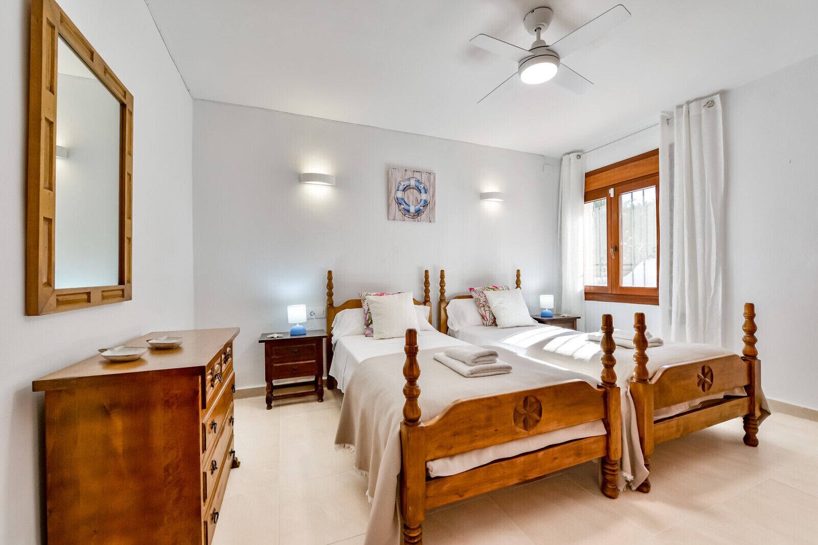 A bedroom with a wooden bed, a dresser, a nightstand, a ceiling fan, and a window with curtains.