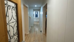 Un pasillo con suelo de madera, paredes blancas y una puerta con detalles metálicos decorativos.