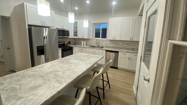 Una cocina moderna con armarios blancos, encimera de mármol e iluminación colgante.
