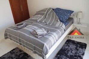 A neatly made bed with striped bedding and pillows, a lamp on a bedside table, and a logo on the wall. - Dar Amira - Dream club in Mahdia / Tunisia modern luxury house-beach close to the beach (Hiboun)