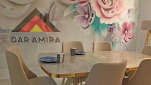 Un salón de conferencias con una mesa de mármol, sillas color beige, un mural floral y el logotipo de 'DAR AMIRA'.