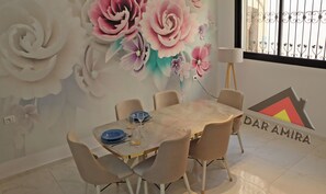 Comedor con una mesa lista para cuatro personas, rodeada de sillas. Se observa un mural en la pared con grandes motivos florales.