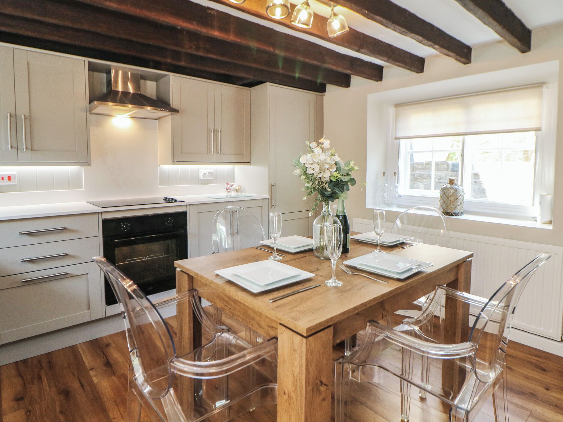 A modern kitchen with wooden flooring, a central island with chairs, and a window with a view.