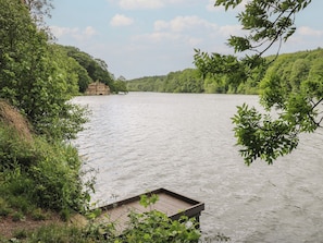 A riverside view with a wooden dock extending into the water, surrounded by lush greenery and a small building on the opposite bank. - Lake Side Cottage (Wakefield)
