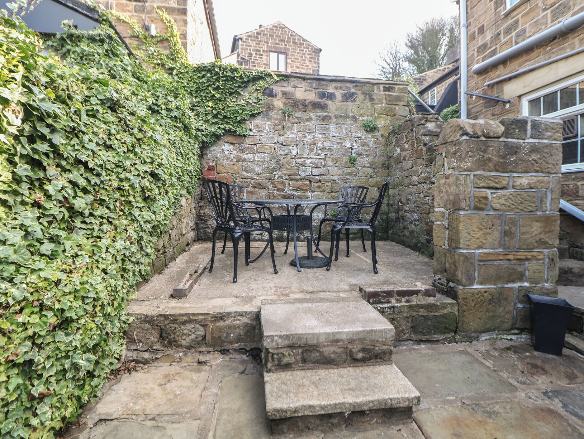 A stone wall with a table and chairs, surrounded by greenery.