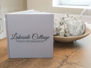 A booklet titled 'Lakeside Cottage Guest Information' on a wooden table with a bowl of artichokes beside it. - Lake Side Cottage (Wakefield)