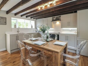 A modern kitchen with wooden flooring, white cabinetry, and a dining table set for four. - Lake Side Cottage (Wakefield)