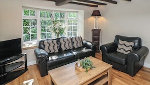 A living room with a black leather sofa, a wooden coffee table, a TV stand, and a lamp. - Lake Side Cottage (Wakefield)