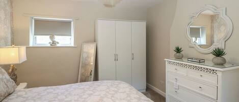 A bedroom with a bed, a dresser, a mirror, a window, and a chandelier.