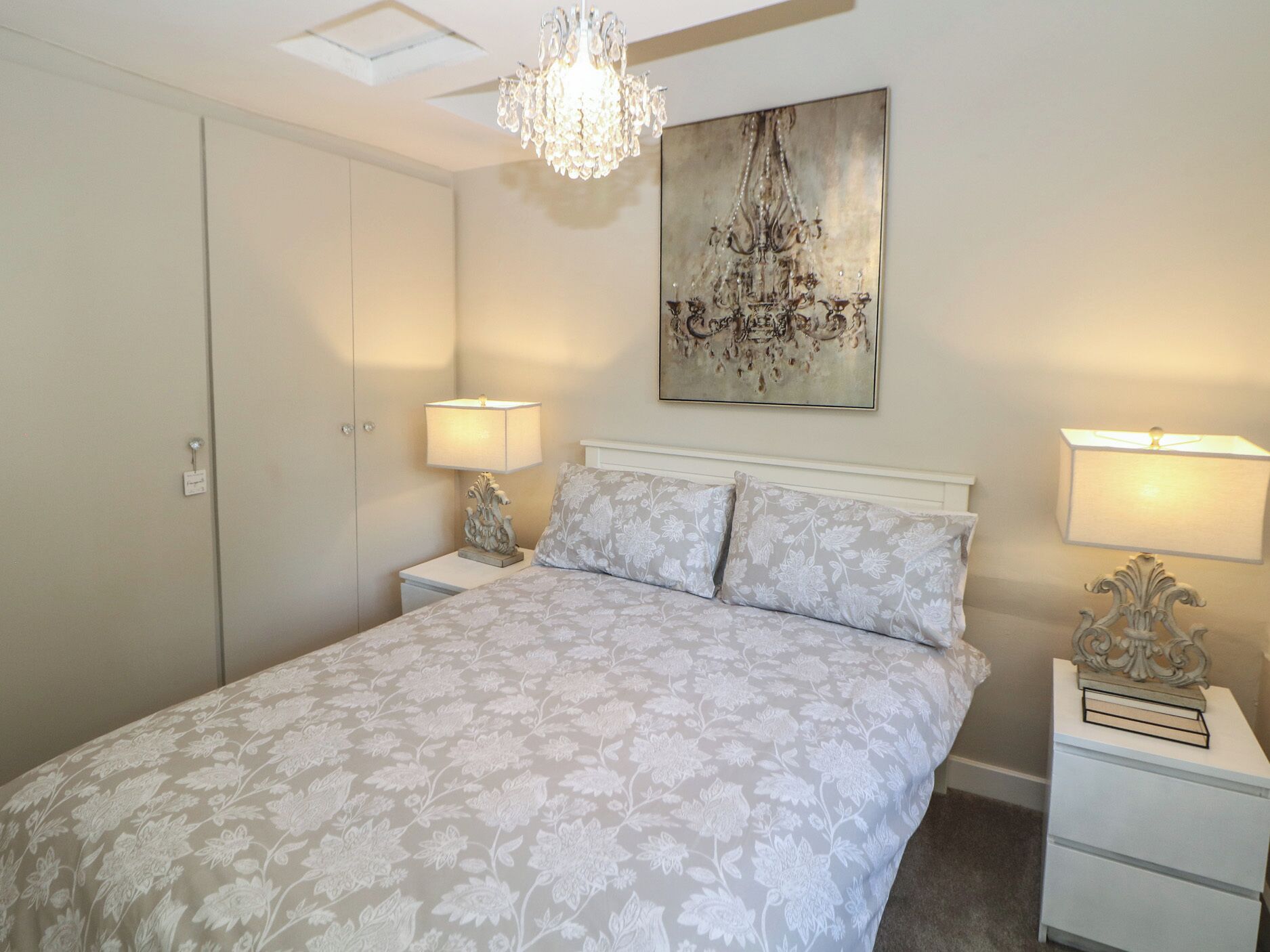 A bedroom with a bed, two bedside tables, a chandelier, and a wall-mounted artwork.