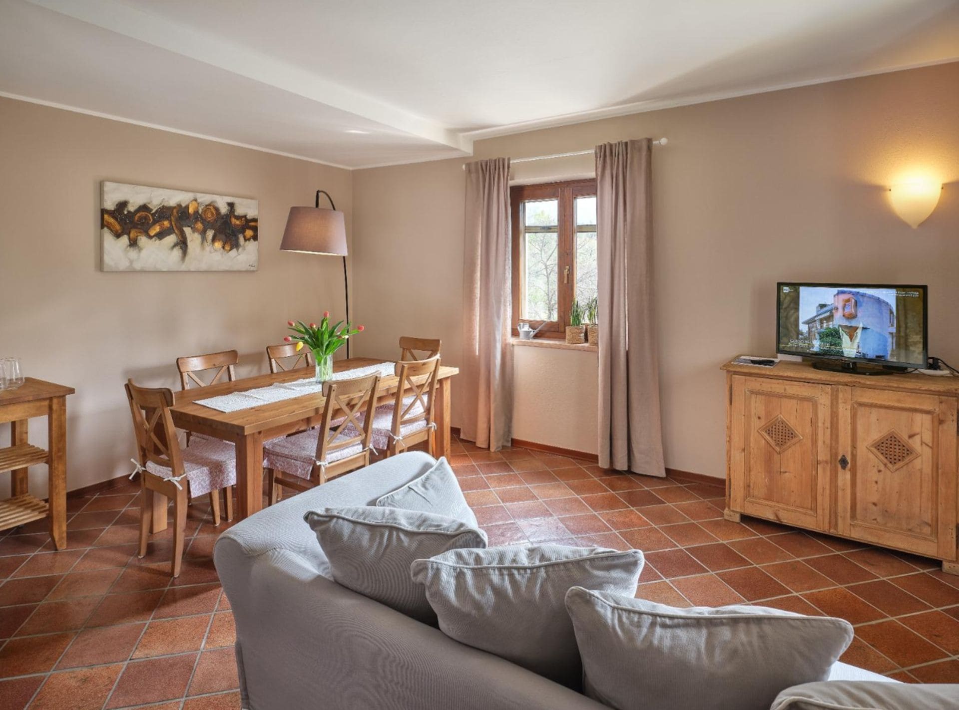 A cozy living room with a sofa, a dining table with chairs, a TV, and a window with curtains.