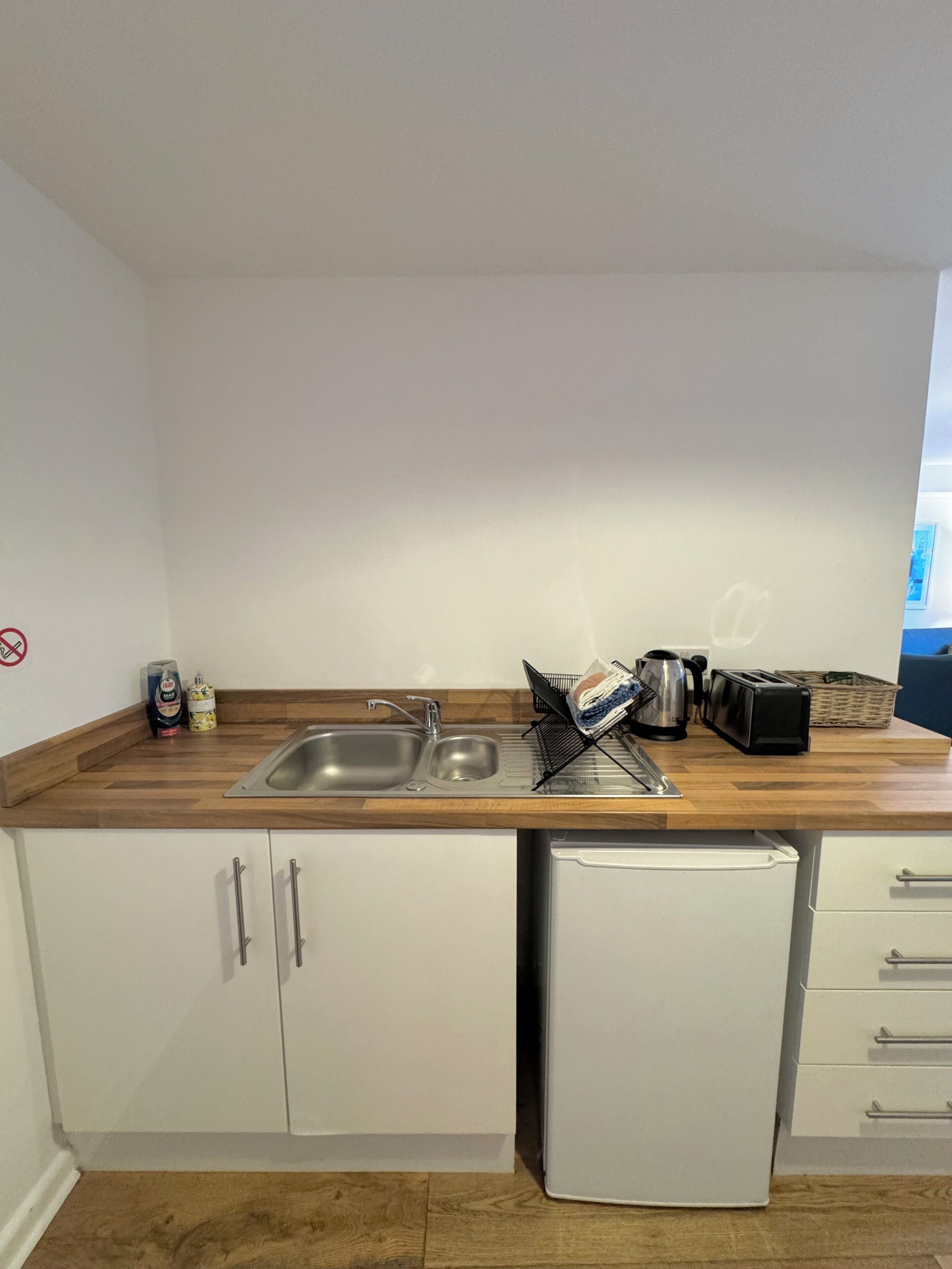 A compact kitchen with a wooden countertop, a sink, a small refrigerator, and white cabinets.