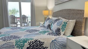 A bedroom with a bed, a ceiling fan, a nightstand with a lamp, a wicker headboard, a white dresser, and a painting on the wall. - BEAUTIFUL GULF VIEW 2B/2B BALCONY OVER THE POOL,EASY BEACH ACCESS (Orange Beach)