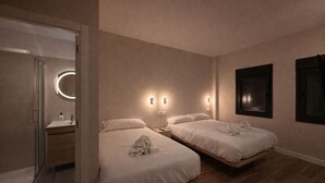 Une chambre d’hôtel avec deux lits, un miroir rond, une petite salle de bain et des lampes fixées au mur.