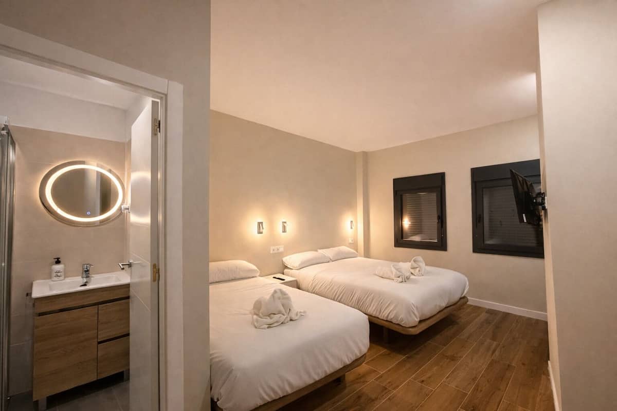A hotel room with a bathroom, two beds, a mirror, and wall-mounted lights.