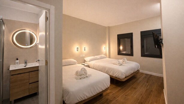 Une chambre d’hôtel avec salle de bain, deux lits, un miroir et des lampes fixées au mur.
