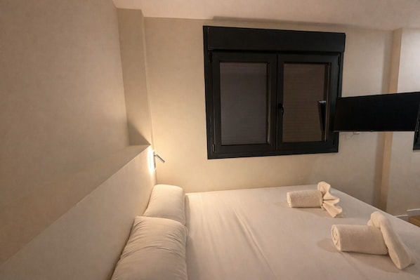 Una habitación de hotel con cama, televisor de pantalla plana en la pared y una mesita de noche.