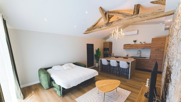 Una camera da letto moderna con un letto, un piccolo tavolo di legno e una kitchenette sullo sfondo.