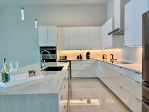 A modern kitchen with white cabinetry, stainless steel appliances, and a marble countertop. - Villa Aesthetic View - great view, on water, pool, spa, gulf access (Cape Coral)