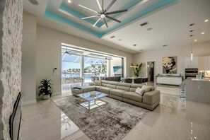 A modern living room with a large sectional sofa, a glass coffee table, and a view of a pool and outdoor seating area. - Villa Aesthetic View - great view, on water, pool, spa, gulf access (Cape Coral)