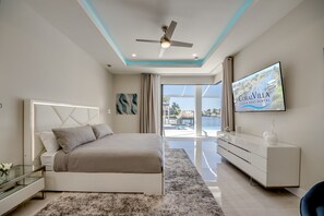 A modern bedroom with a bed, a TV, and a view of the outside. - Villa Aesthetic View - great view, on water, pool, spa, gulf access (Cape Coral)