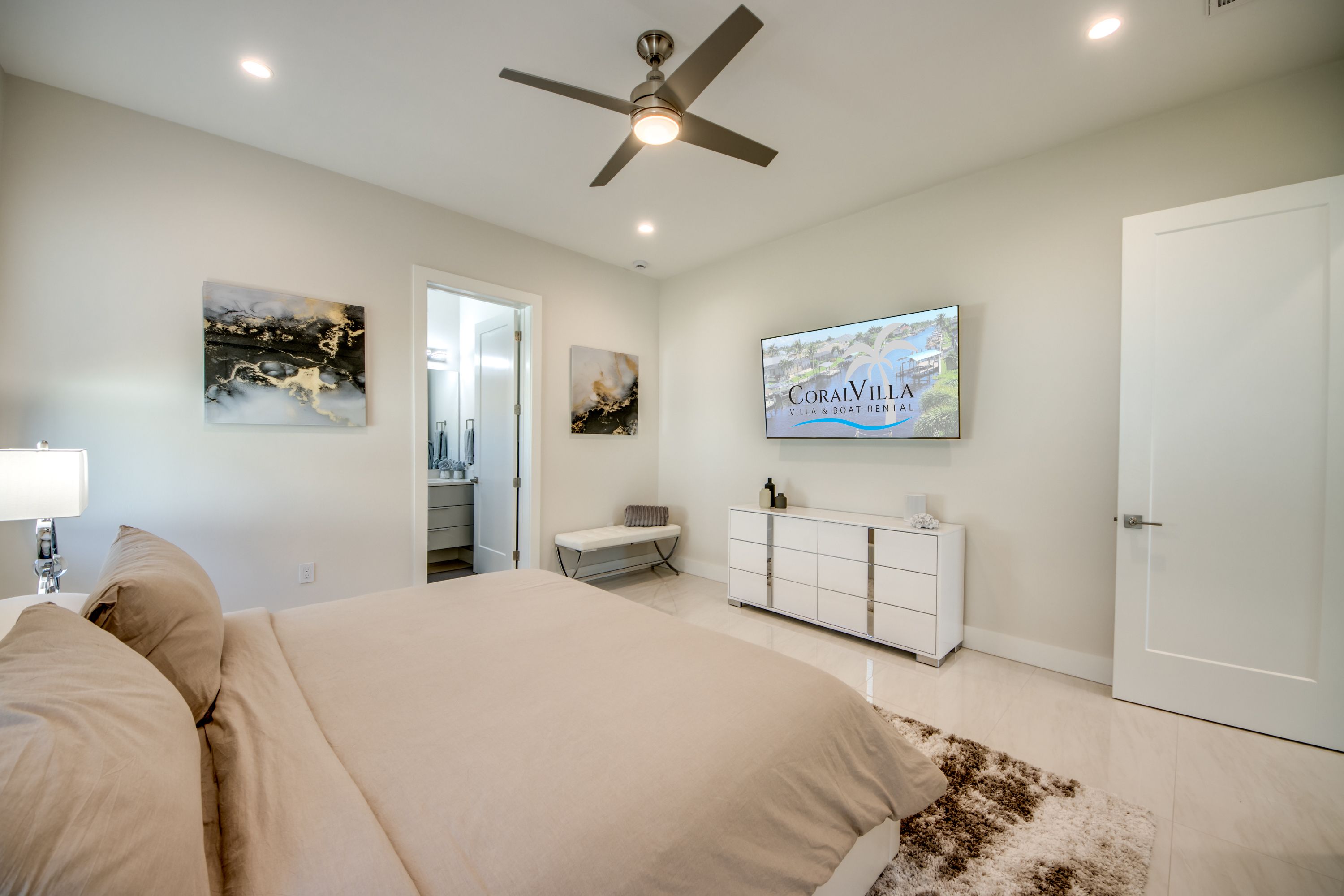A bedroom with a bed, a ceiling fan, a TV, and artwork on the walls.