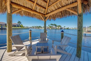 A wooden deck with lounge chairs and a table, overlooking a body of water with a thatched roof overhead. - Villa Aesthetic View - great view, on water, pool, spa, gulf access (Cape Coral)
