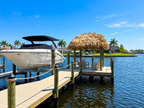 A boat docked at a pier with a thatched-roof structure nearby. - Villa Aesthetic View - great view, on water, pool, spa, gulf access (Cape Coral)