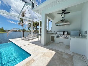 A poolside area with a view of the water, a grill, and lounge chairs. - Villa Aesthetic View - great view, on water, pool, spa, gulf access (Cape Coral)