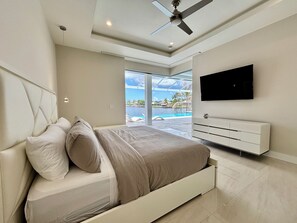 A modern bedroom with a bed, a TV, and a view of a pool. - Villa Aesthetic View - great view, on water, pool, spa, gulf access (Cape Coral)