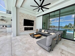 A modern living room with a large TV, a sofa, and a view of a swimming pool. - Villa Aesthetic View - great view, on water, pool, spa, gulf access (Cape Coral)