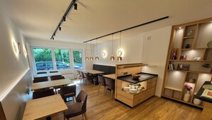 A modern restaurant with wooden tables and chairs, a central island with a sink, and pendant lighting. - Hotel Wilms (Cologne)