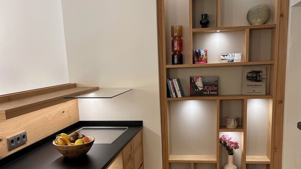 A modern kitchen with a wooden countertop, built-in storage, and a wooden shelving unit with decorative items. - Hotel Wilms (Cologne)