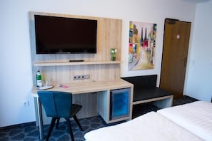 Een hotelkamer met een bed, een bureau met stoel, een aan de muur bevestigde televisie en een schilderij.