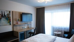 A hotel room with a bed, a desk with a TV, a small table, and a chair. - Hotel Wilms (Cologne)