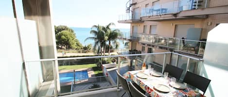 A balcony with a table set for two, overlooking a swimming pool and a view of the sea.